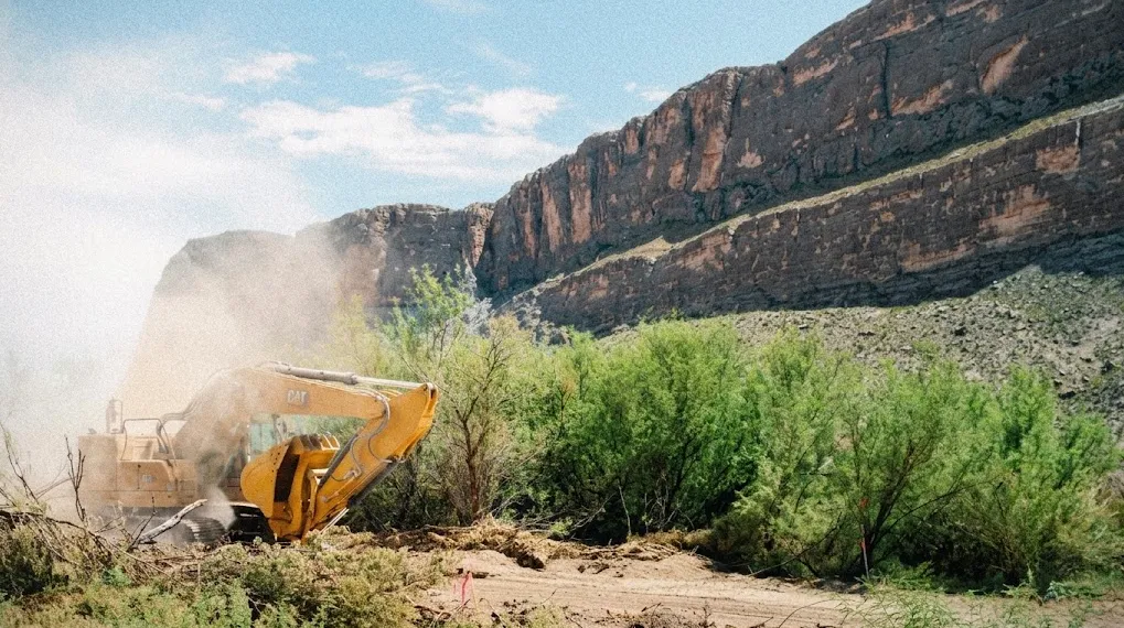 An excavator clearing brush below the canyon cliffs of Big Bend