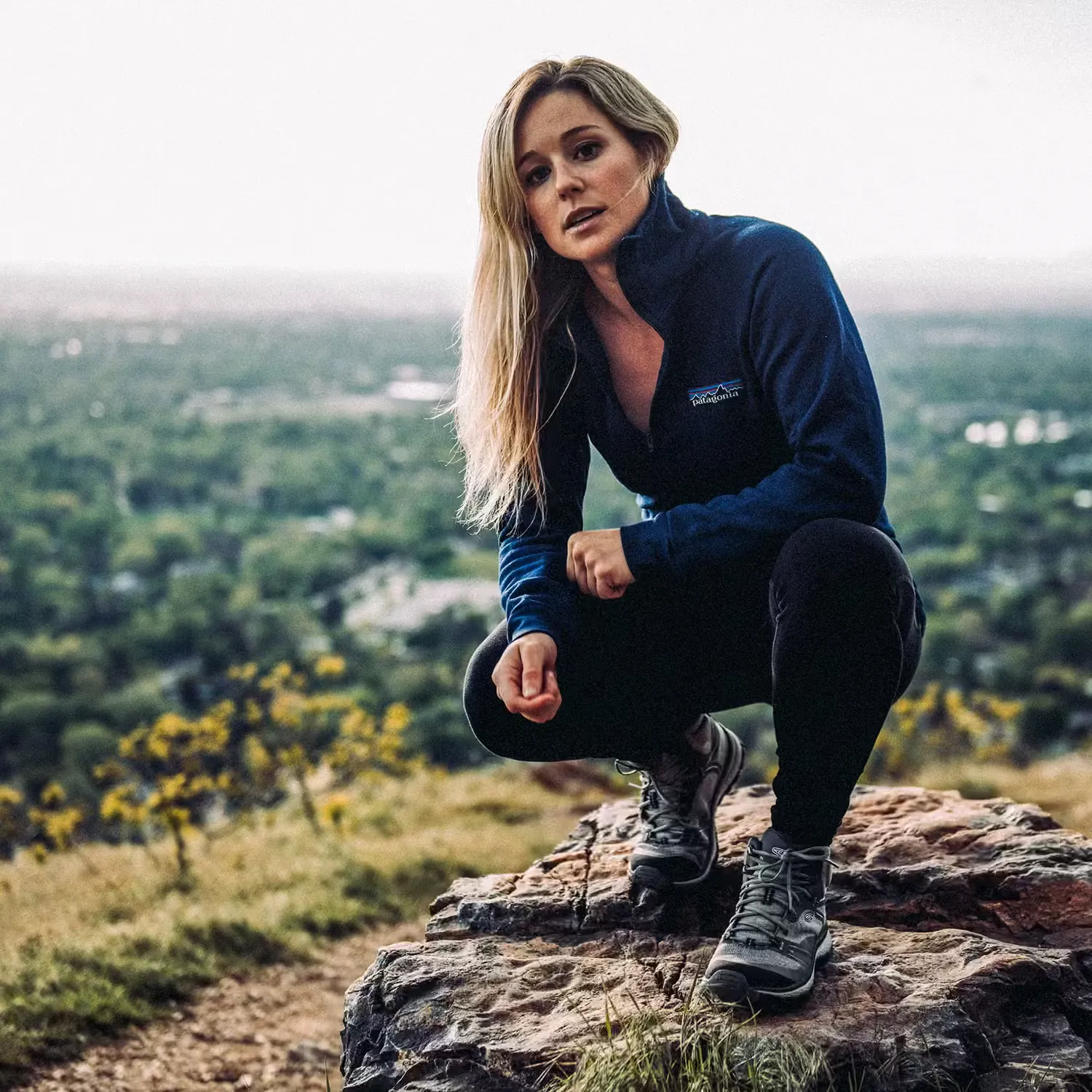 Caroline Gleich crouching on a rock above a green valley