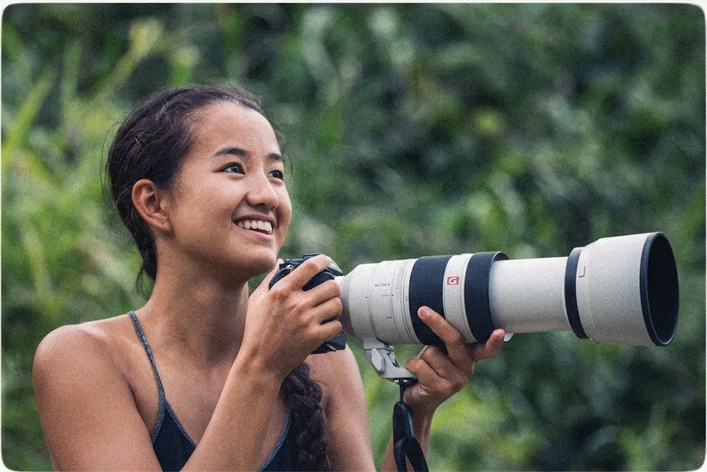 Celina Chien smiling behind a camera with a long telephoto lens